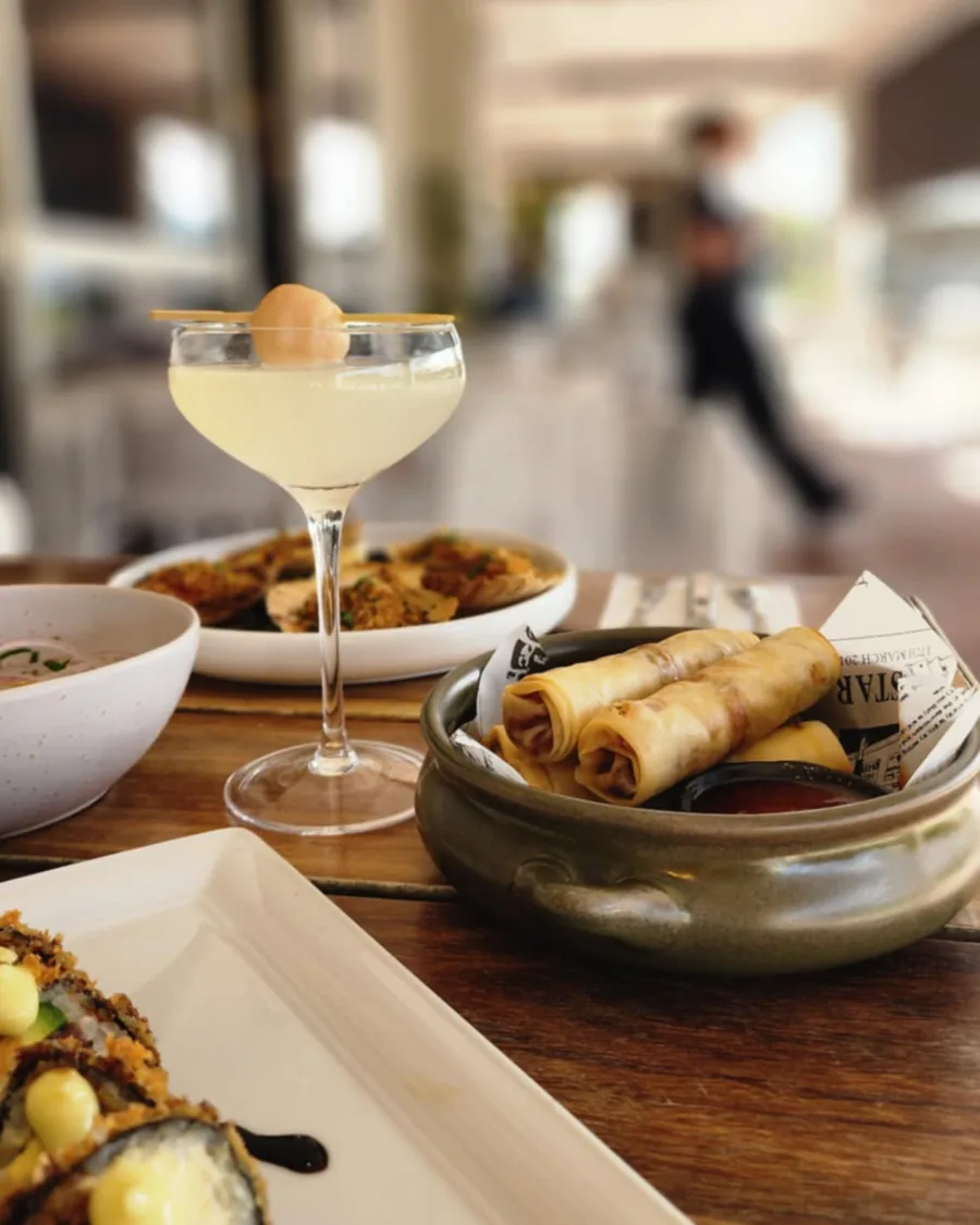 Share plates and a cocktail on a table in the dining room, with service moving behind