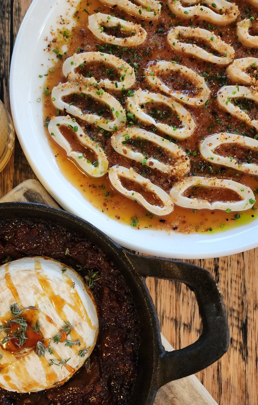 Salt and pepper calamari and a baked camembert in a cast-iron skillet on a timber table
